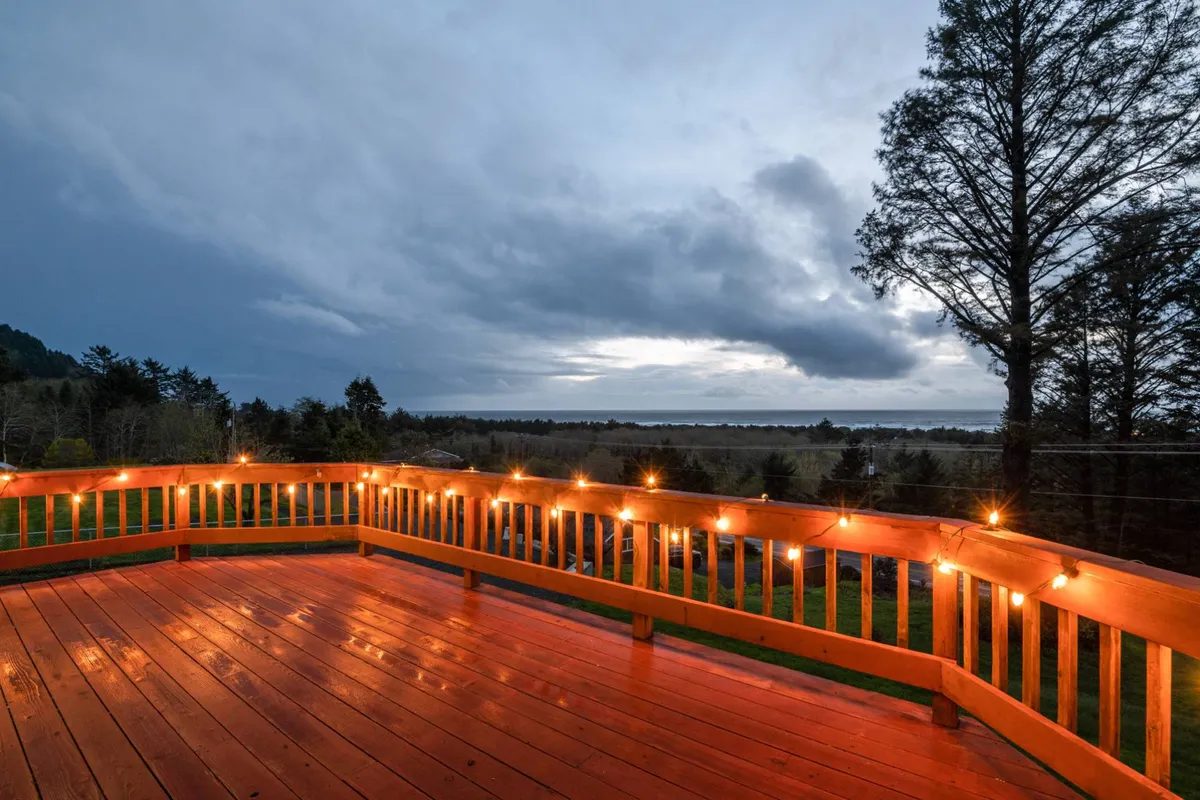 This exterior shot captures a wooden deck adorned with string lights, looking out onto a distant horizon. The tranquil setting suggests a relaxing spot for both people and their pets to unwind after a day of outdoor adventures, with the open sky and natural scenery reinforcing the coastal atmosphere.