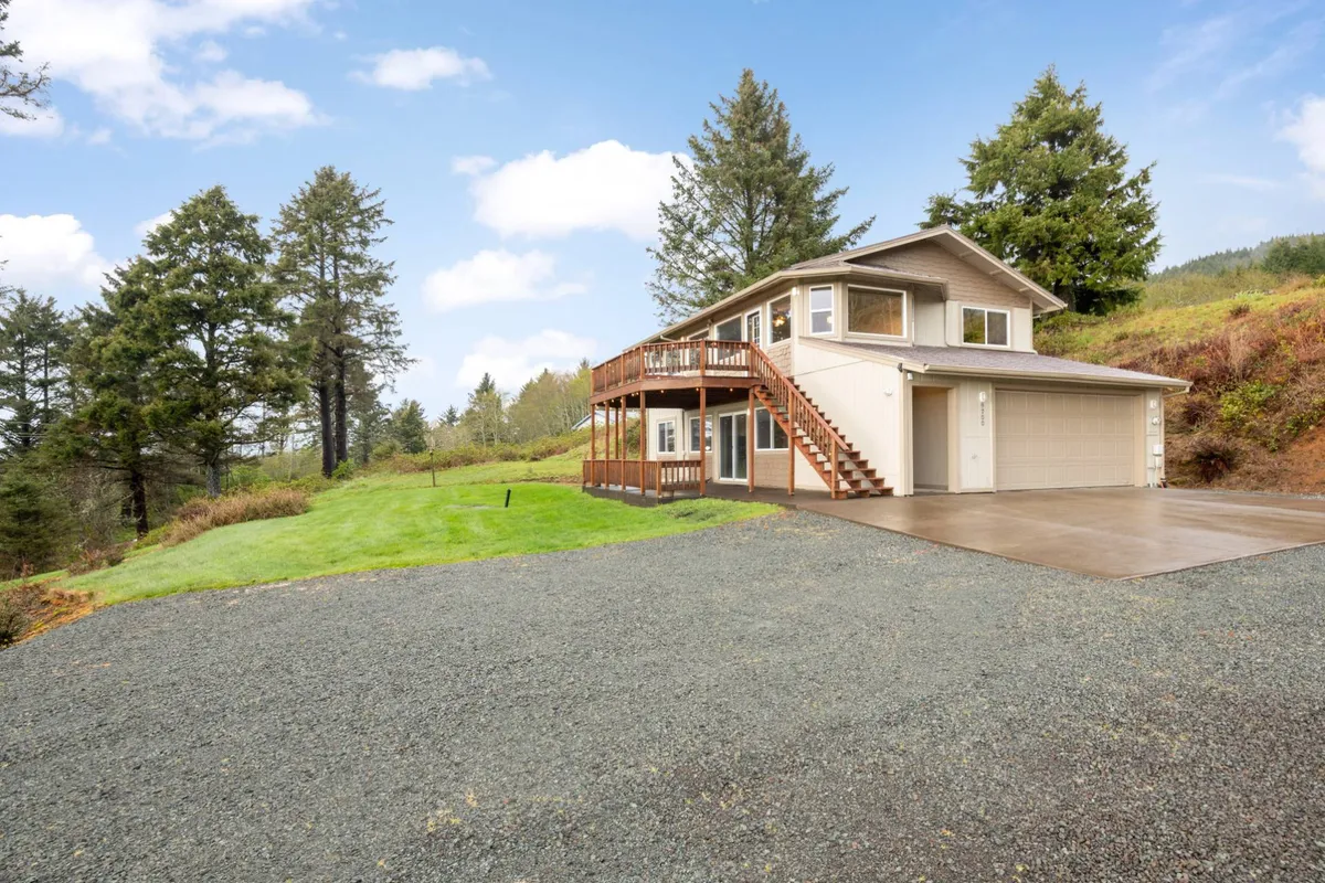 This image showcases the exterior of Casa Del Sol, focusing on a spacious lawn in front of the house, framed by a tree line and a gravel driveway. The balcony and open green area signal ample space for pets and children to play safely outdoors.