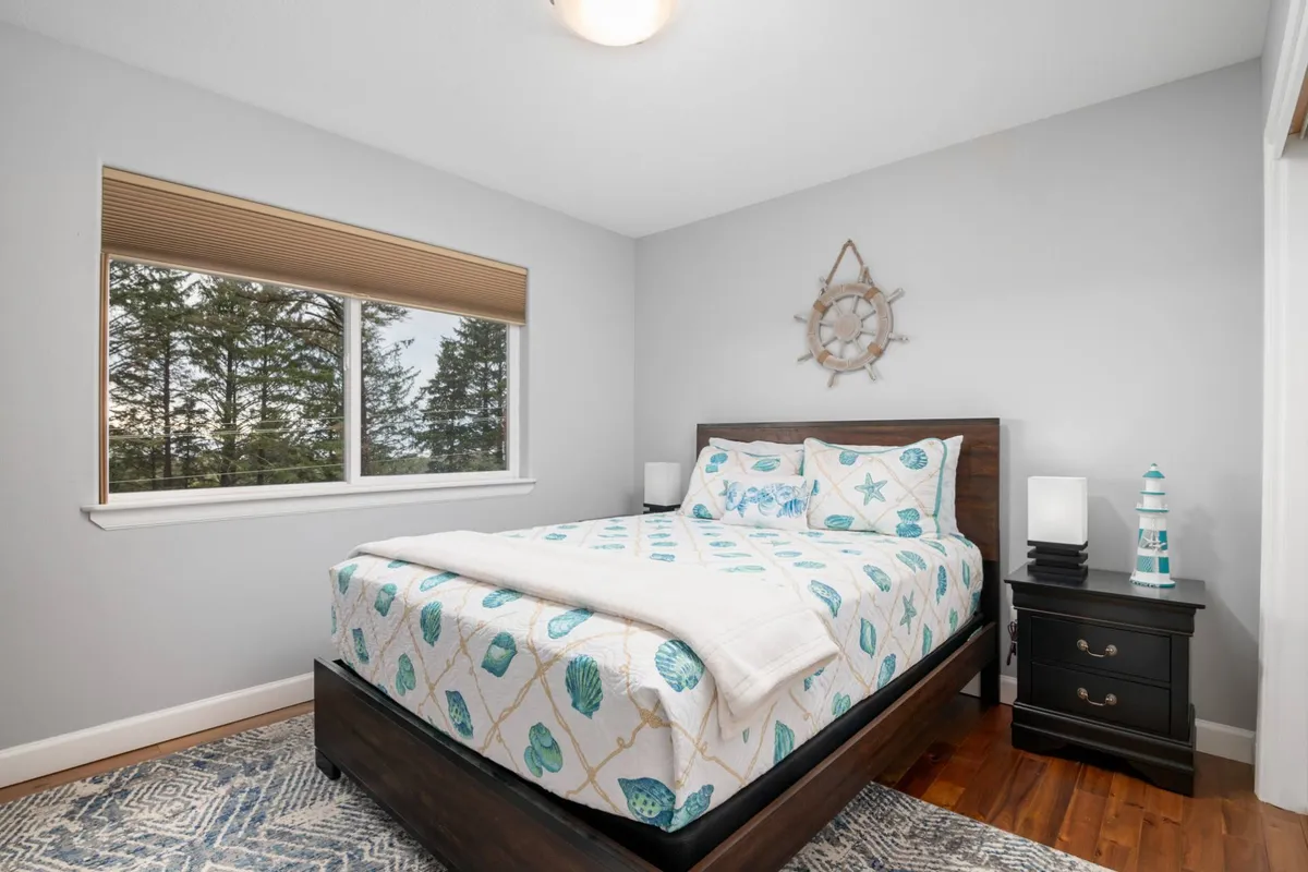 A serene interior featuring a bed with sea-themed bedding and a window offering a glimpse of the surrounding forest. The room feels peaceful and restorative, perfect for relaxing with your pet after a day of exploring beaches and green spaces.