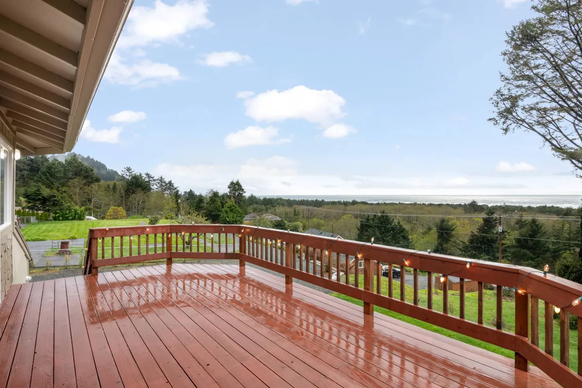 An upper wooden deck overlooking the ocean and lush green landscape. The setting is tranquil and perfect for outdoor dining, relaxation, or simply soaking in the panoramic views—ideal for sunrise coffee or sunset toasts.