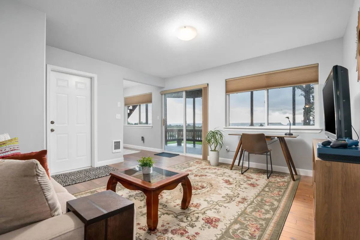 A comfortable living area featuring a sofa, coffee table, large windows framing ocean views, and a dedicated desk with a monitor. The arrangement is perfect for relaxing, entertaining, or productive remote work—all with an inspiring backdrop.