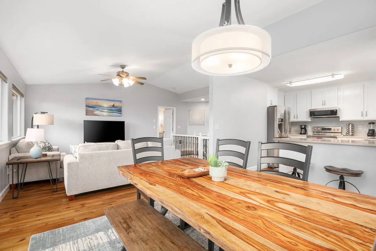 An inviting open-concept interior highlighting a spacious dining table, adjacent seating area, and a modern kitchen. Large windows suggest abundant natural light and hint at picturesque views, making this an ideal setting for both everyday living and entertaining guests.