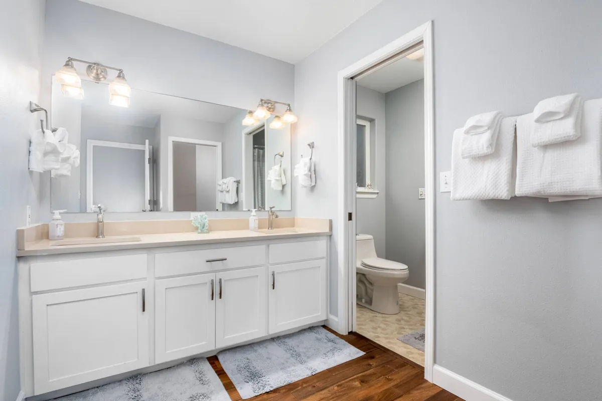 A fresh and inviting bathroom scene with a modern vanity, large mirror, bright lighting fixtures, and neatly arranged towels. The clean lines and subtle décor evoke a spa-like feel.