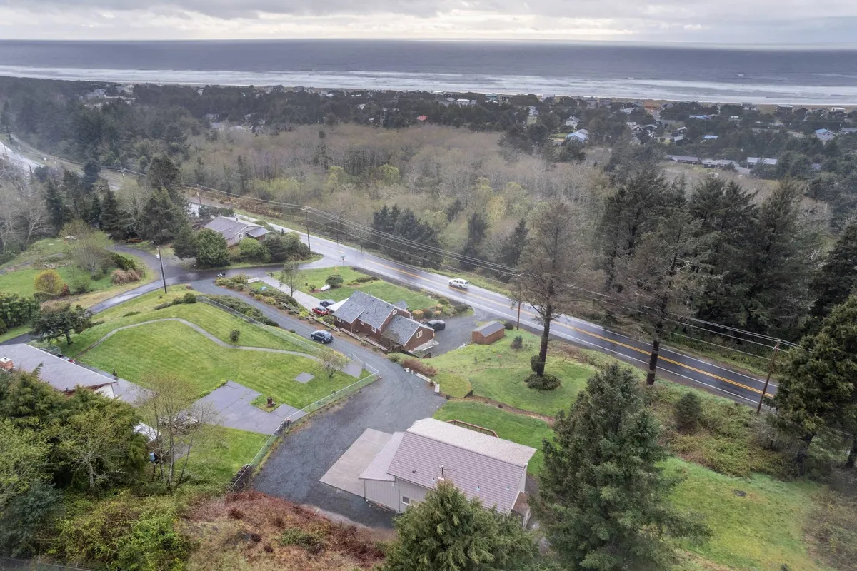 A sweeping view of the coastline, with the ocean, lush greenery, a winding roadway, and the local neighborhood layout visible. The scene conjures images of scenic drives, walks, and a peaceful coastal atmosphere awaiting exploration.