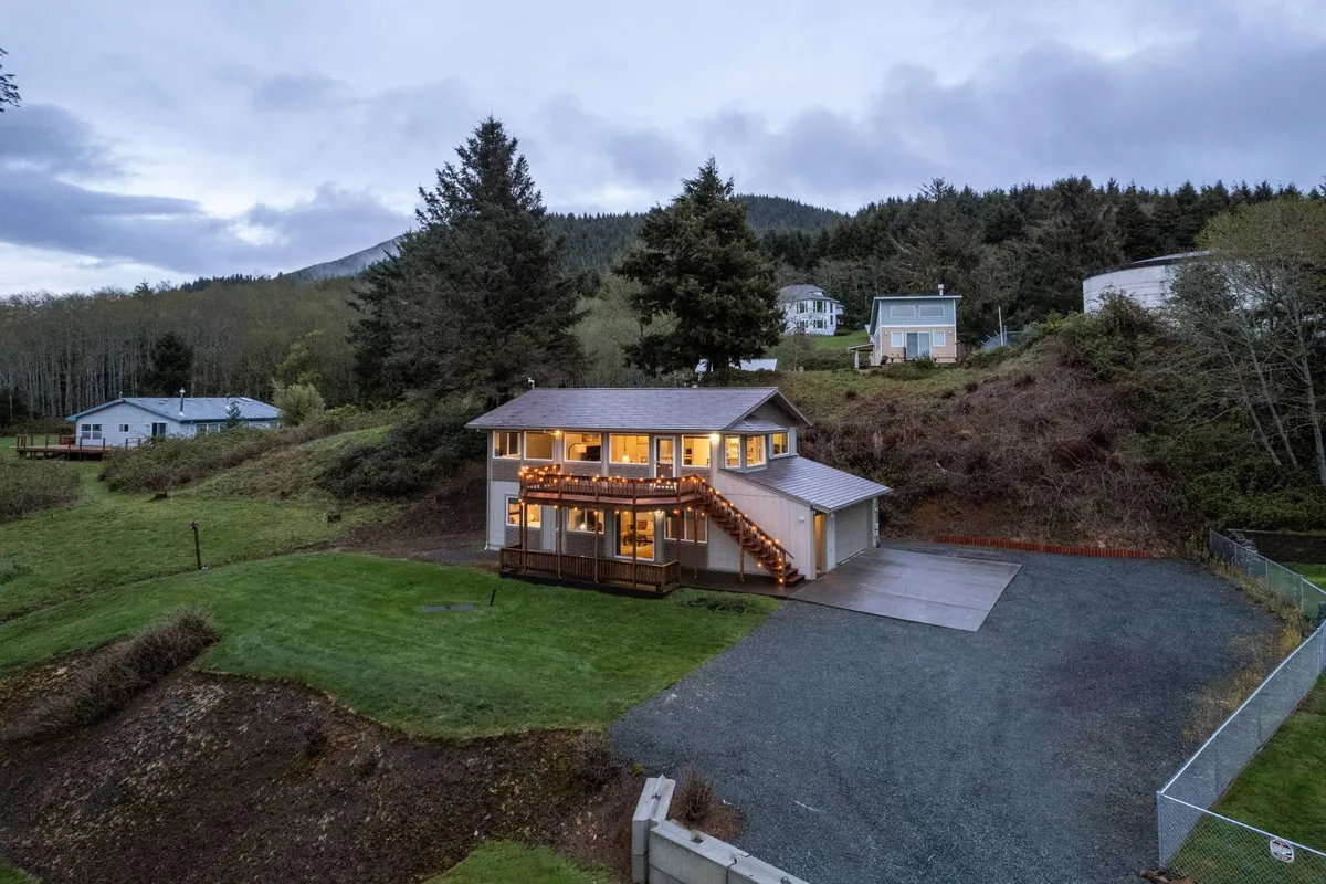 An inviting exterior shot of Casa Del Sol, featuring the house, a spacious deck, driveway for ample parking, and lush surrounding trees. The welcoming outdoor space hints at family gatherings, pet-friendly fun, and a place to unwind after a day at the beach.